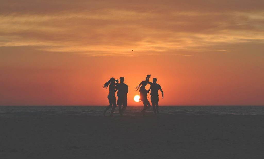 Des amis dansent sur la plage pendant que le soleil se couche